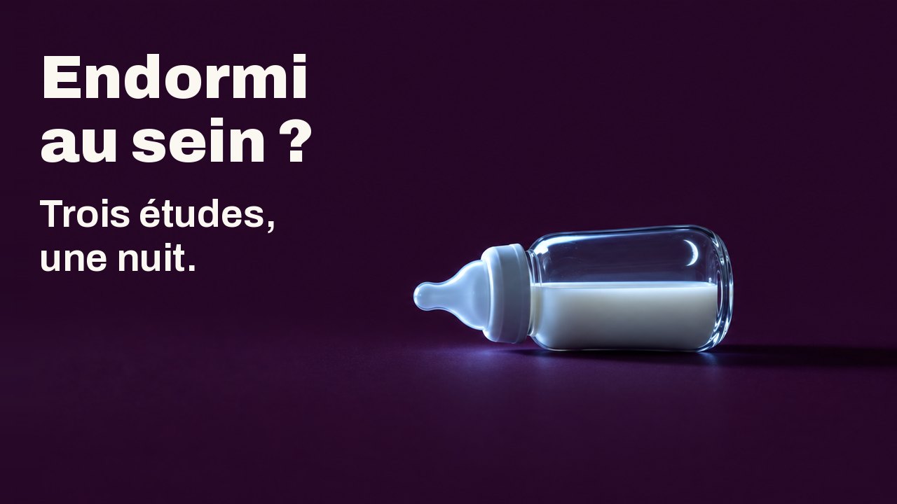 Endormi au sein ? Trois études, une nuit. Un petit biberon en verre rempli de lait est couché sur le côté sur un fond prune profond, éclairé d’un côté par la lumière froide d’un écran invisible, un fin croissant de lune se reflétant dans le verre.