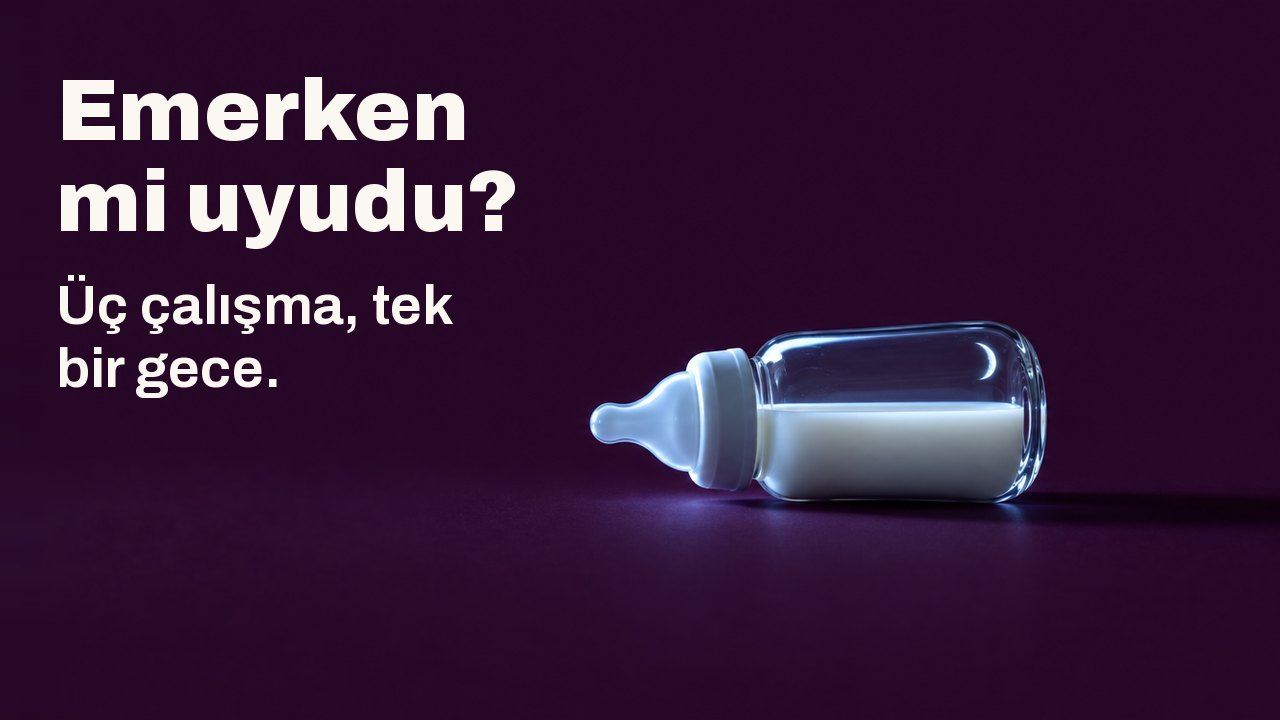 Emerken mi uyudu? Üç çalışma, tek bir gece. Sütle dolu küçük cam bir biberon koyu erik rengi bir zeminde yan yatmış, bir yandan görünmeyen bir ekranın soğuk ışığıyla aydınlanıyor, camda ince bir hilal yansıyor.