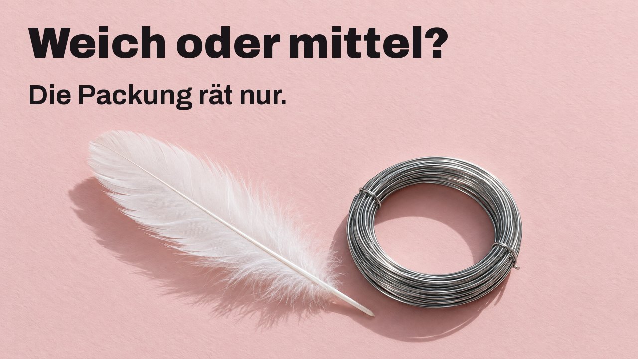 Weich oder mittel? Die Packung rät nur. Von oben: eine weiche weiße Feder neben einer festen Rolle steifen Stahldrahts auf zartrosa Papier.