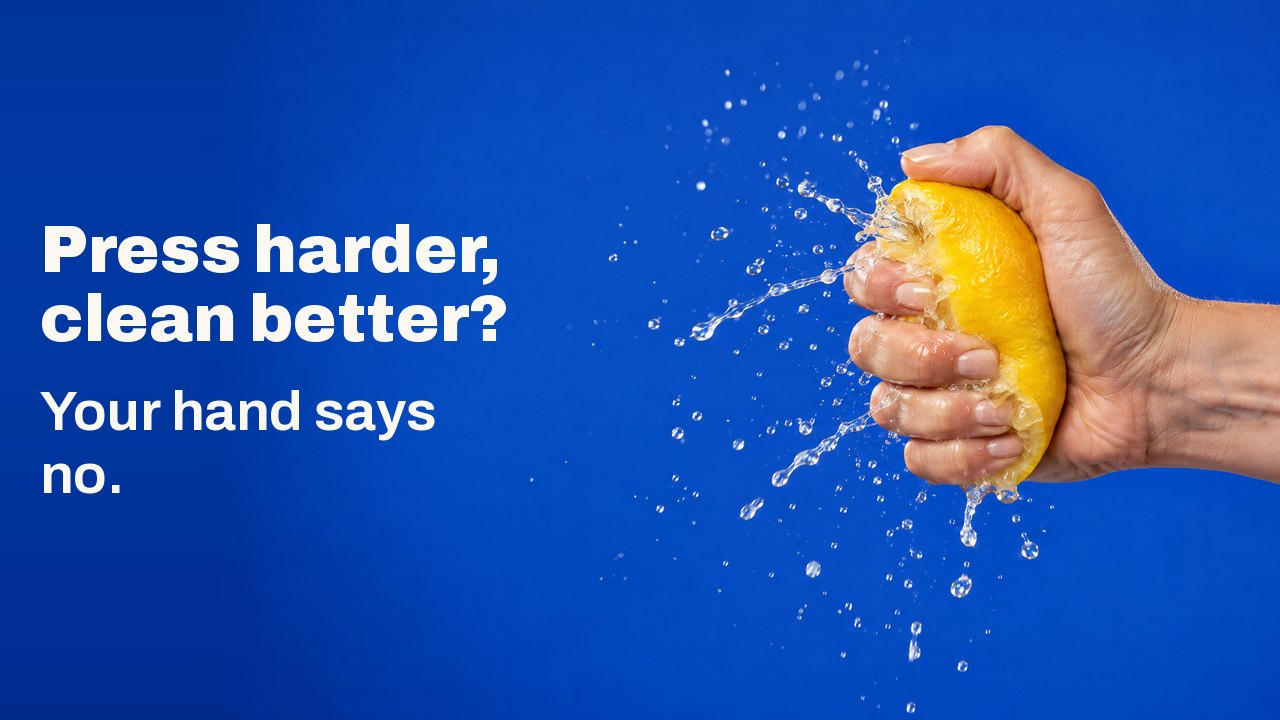 Press harder, clean better? Your hand says no. A hand squeezing a lemon so hard that juice bursts out in a frozen spray, against cobalt blue.