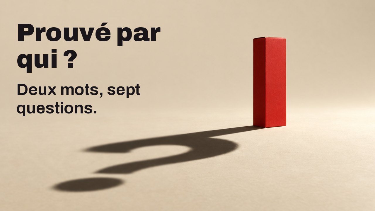 Prouvé par qui ? Deux mots, sept questions. Une simple boîte rouge mate sans aucune inscription se dresse sur un sol crème chaleureux sous un seul projecteur dur et rasant ; sa longue ombre nette sur le sol dessine un point d’interrogation.