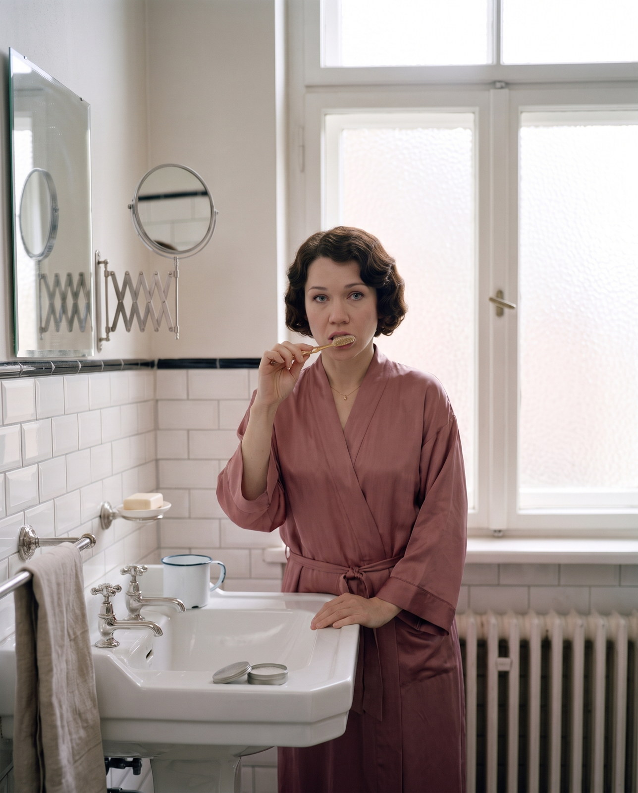 The future of oral health: a woman with a 1920s finger waved bob brushes her teeth with a celluloid brush and tooth powder at a pedestal basin in a 1925 Berlin bathroom