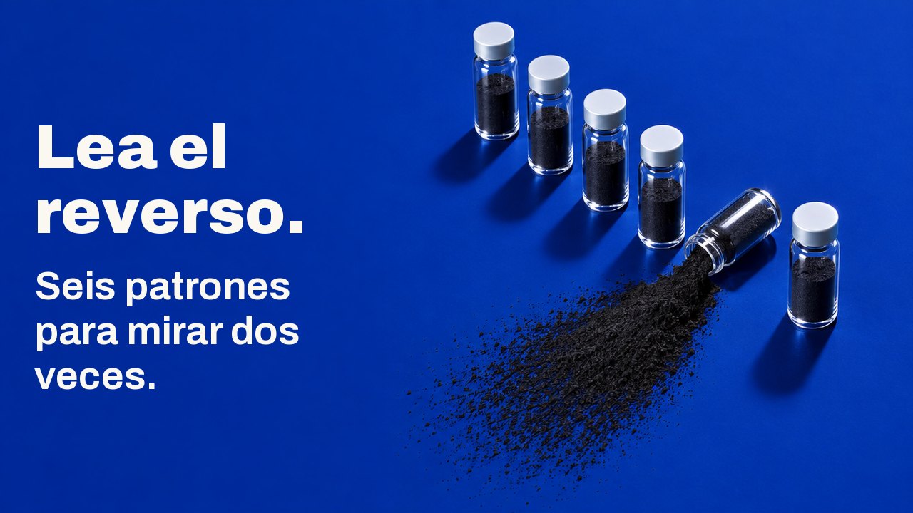 Lea el reverso. Seis patrones para mirar dos veces. Visto desde arriba sobre una superficie azul cobalto intenso: seis frasquitos de cristal en fila, y uno volcado que derrama un abanico de polvo de carbón negro.