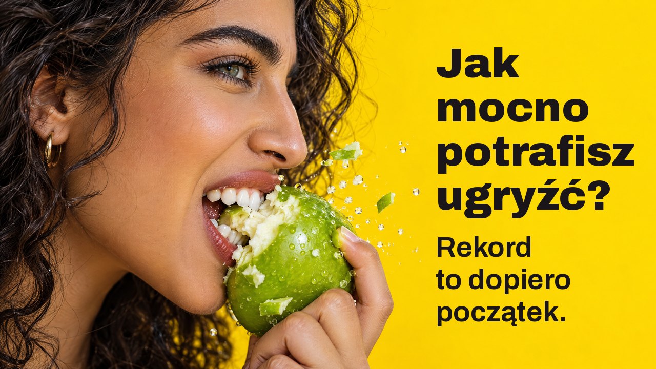 Jak mocno potrafisz ugryźć? Rekord to dopiero początek. Zbliżenie z profilu: kobieta mocno wgryza się w chrupiące zielone jabłko, odpryski lecą, na jaskrawożółtym tle.