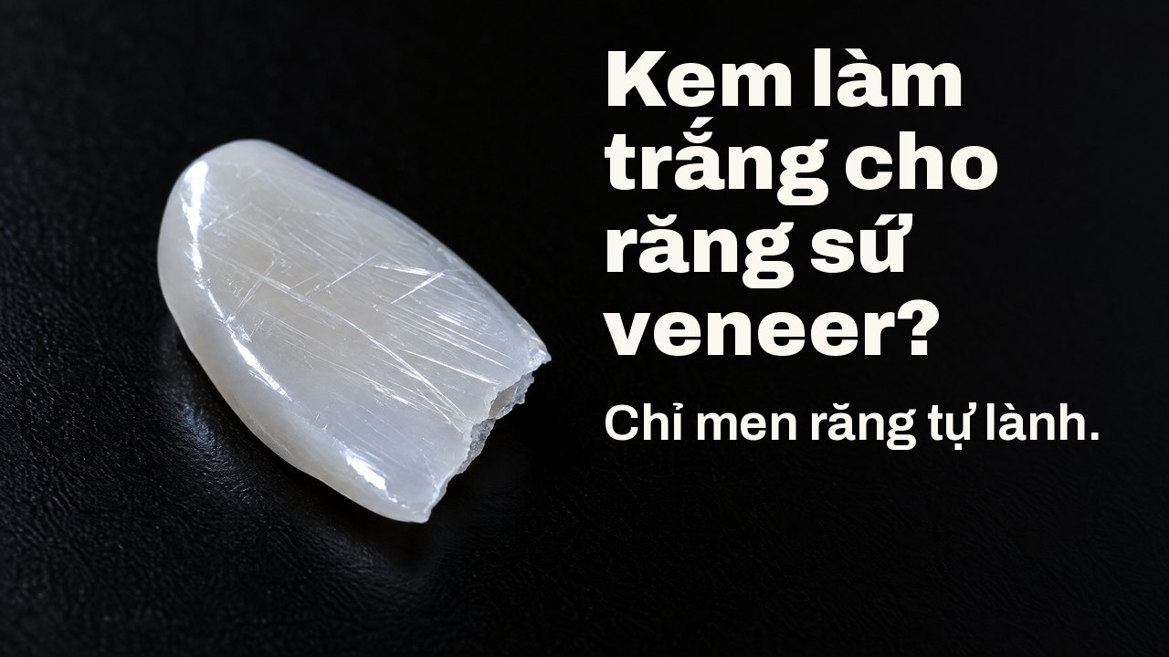 Kem làm trắng cho răng sứ veneer? Chỉ men răng tự lành. Dưới ánh sáng xiên: mảnh sứ mỏng bóng như veneer, bề mặt chằng chịt vết xước nhỏ, trên nền đen.