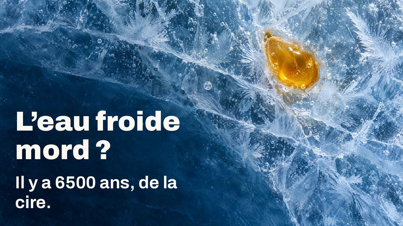 L’eau froide mord ? Il y a 6500 ans, de la cire. Vu d’en haut : une goutte de cire d’abeille dorée prise dans une glace bleue fissurée, avec des fleurs de givre et des bulles d’air.
