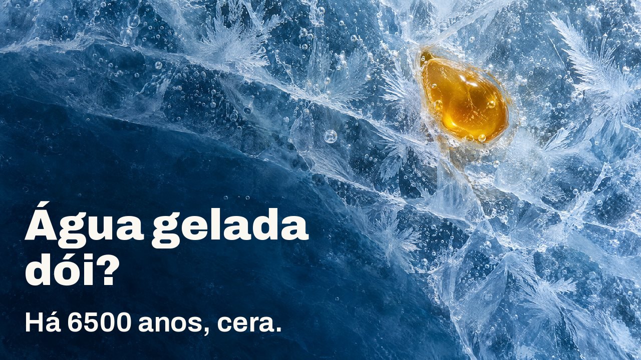 Água gelada dói? Há 6500 anos, cera. Visto de cima: uma gota de cera de abelha dourada presa em gelo azul rachado, com flores de geada e bolhas de ar.