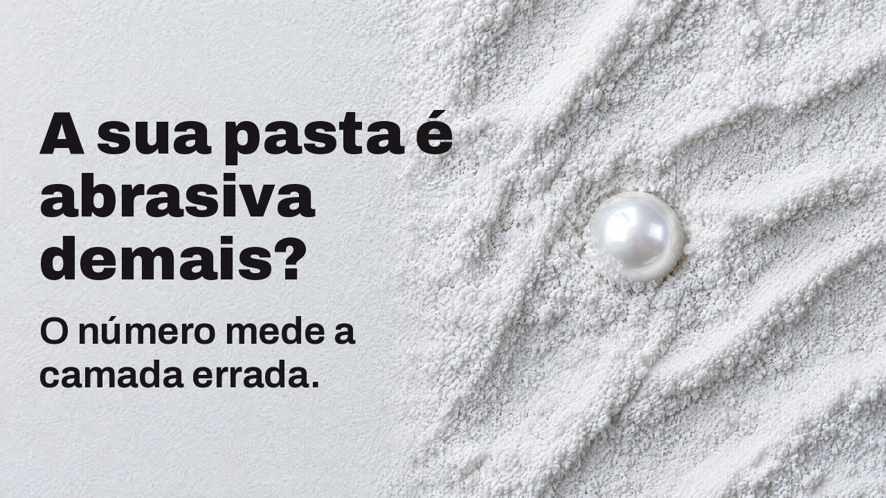 A sua pasta é abrasiva demais? O número mede a camada errada. Visto de cima: uma única pérola brilhante meio enterrada em pó abrasivo branco e fino.
