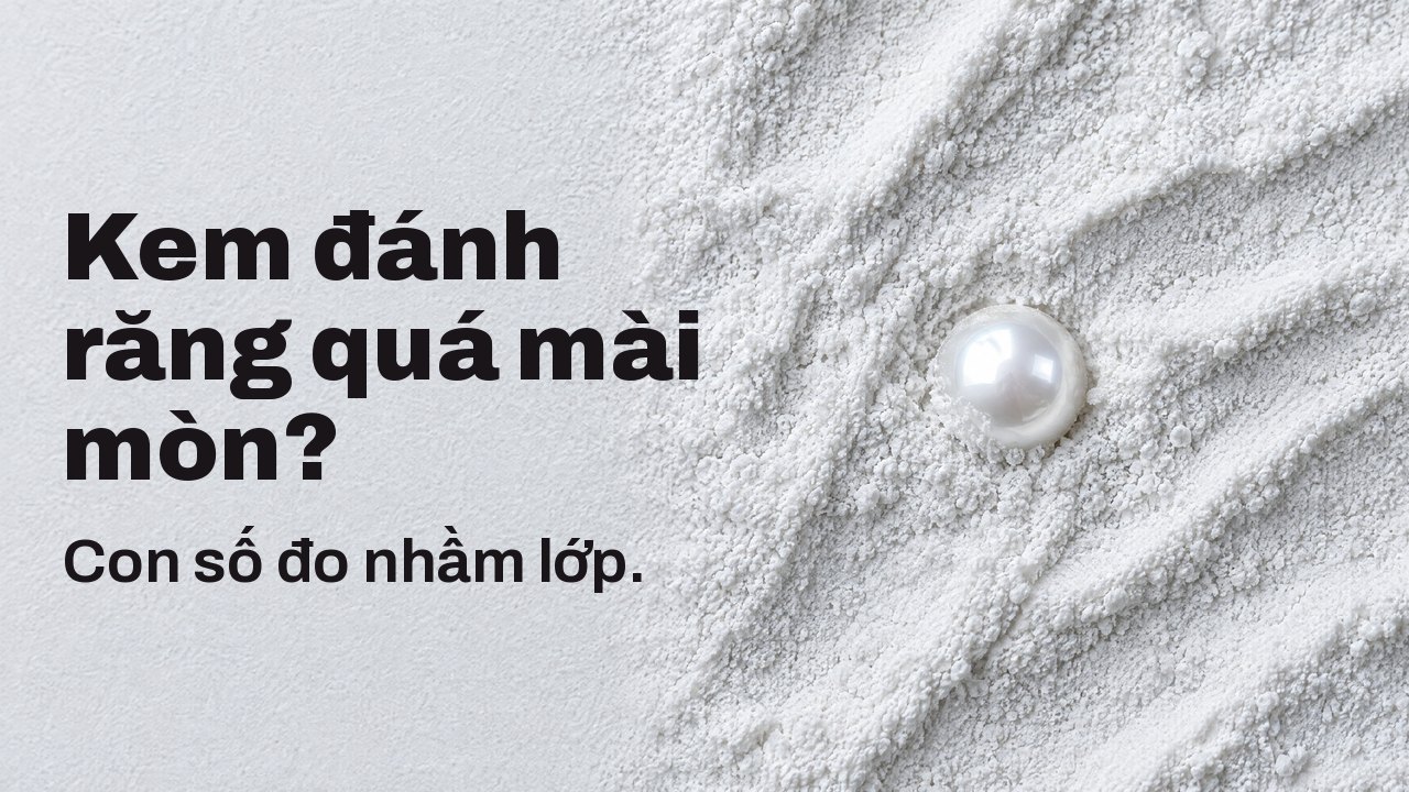 Kem đánh răng quá mài mòn? Con số đo nhầm lớp. Nhìn từ trên: một viên ngọc trai bóng lấp nửa trong lớp bột mài mòn trắng mịn.