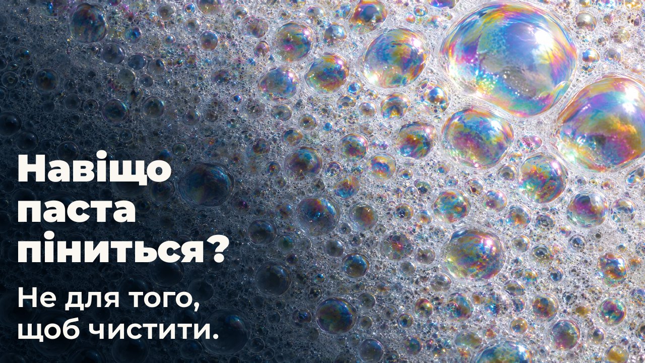 Навіщо паста піниться? Не для того, щоб чистити. Макро білої піни: безліч дрібних бульбашок із райдужною плівкою, кілька великих ловлять світло.