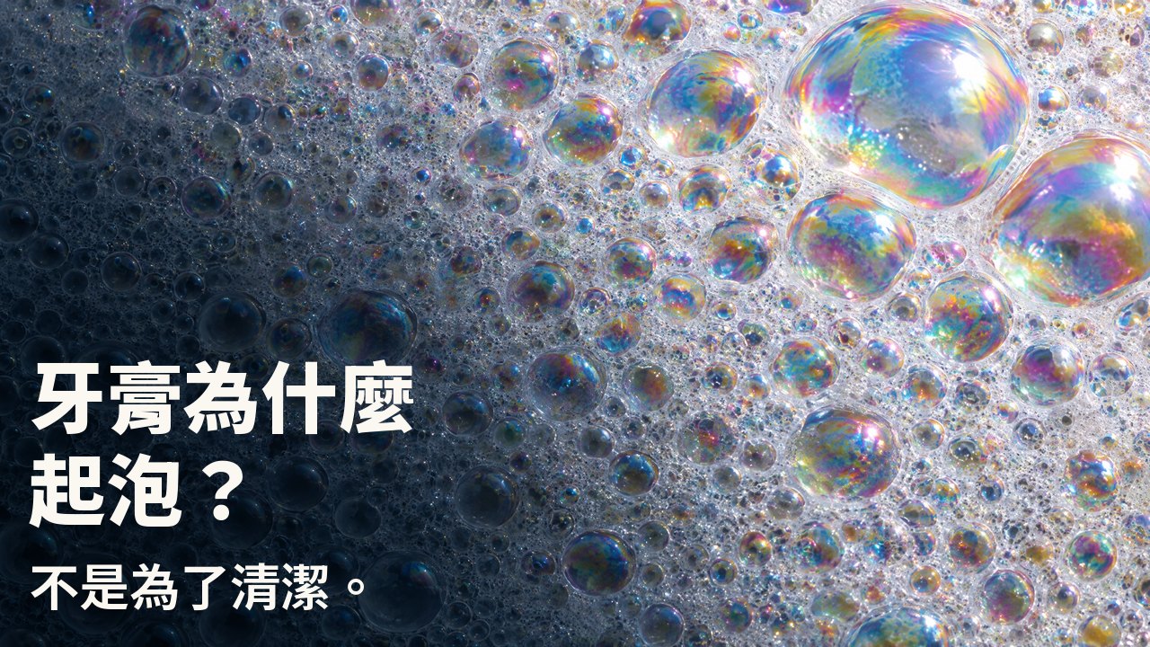 牙膏為什麼起泡？ 不是為了清潔。 白色泡沫微距：無數帶彩虹虹彩膜的小泡泡，幾顆大泡泡映著光。